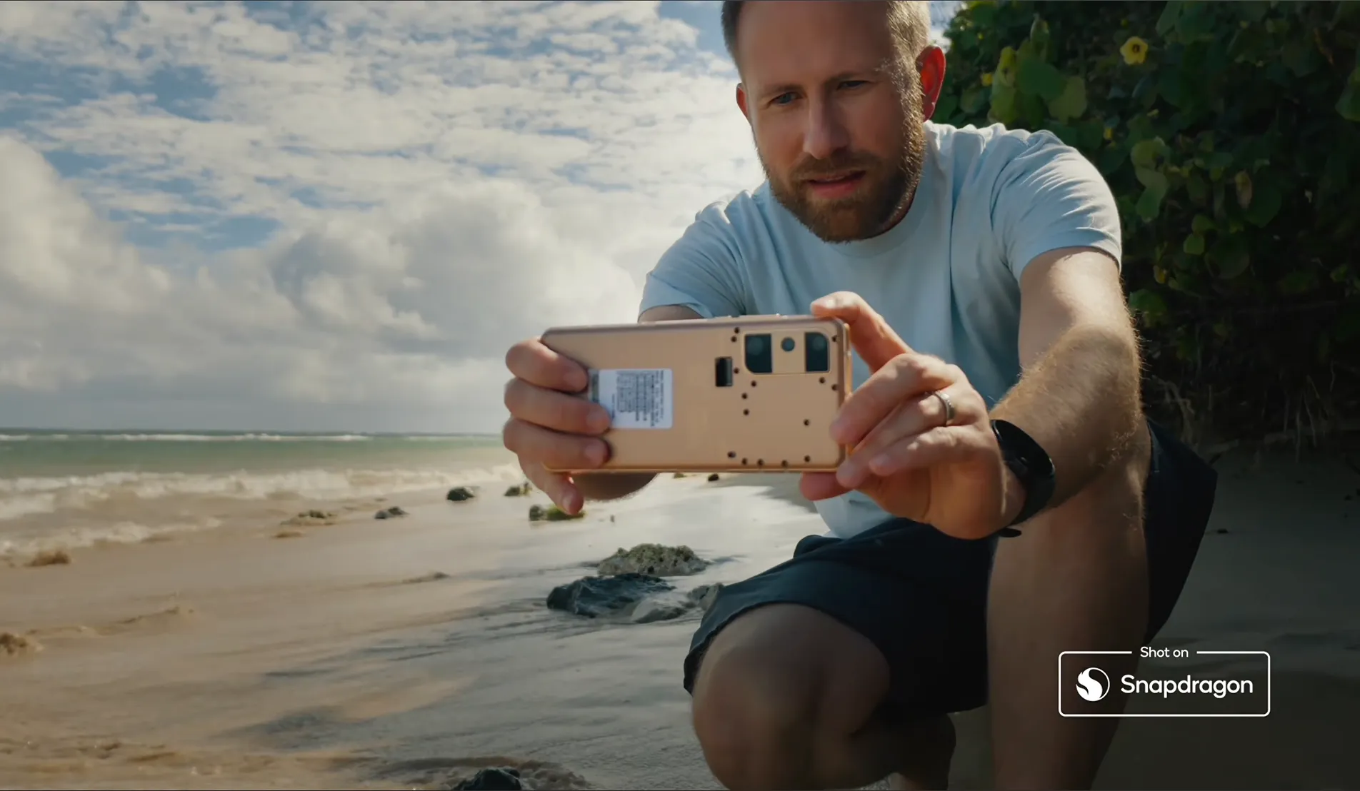 Joshua Timothy crouched down on the beach filming videos with a Qualcomm Reference Devices featuring the latest Snapdragon chip