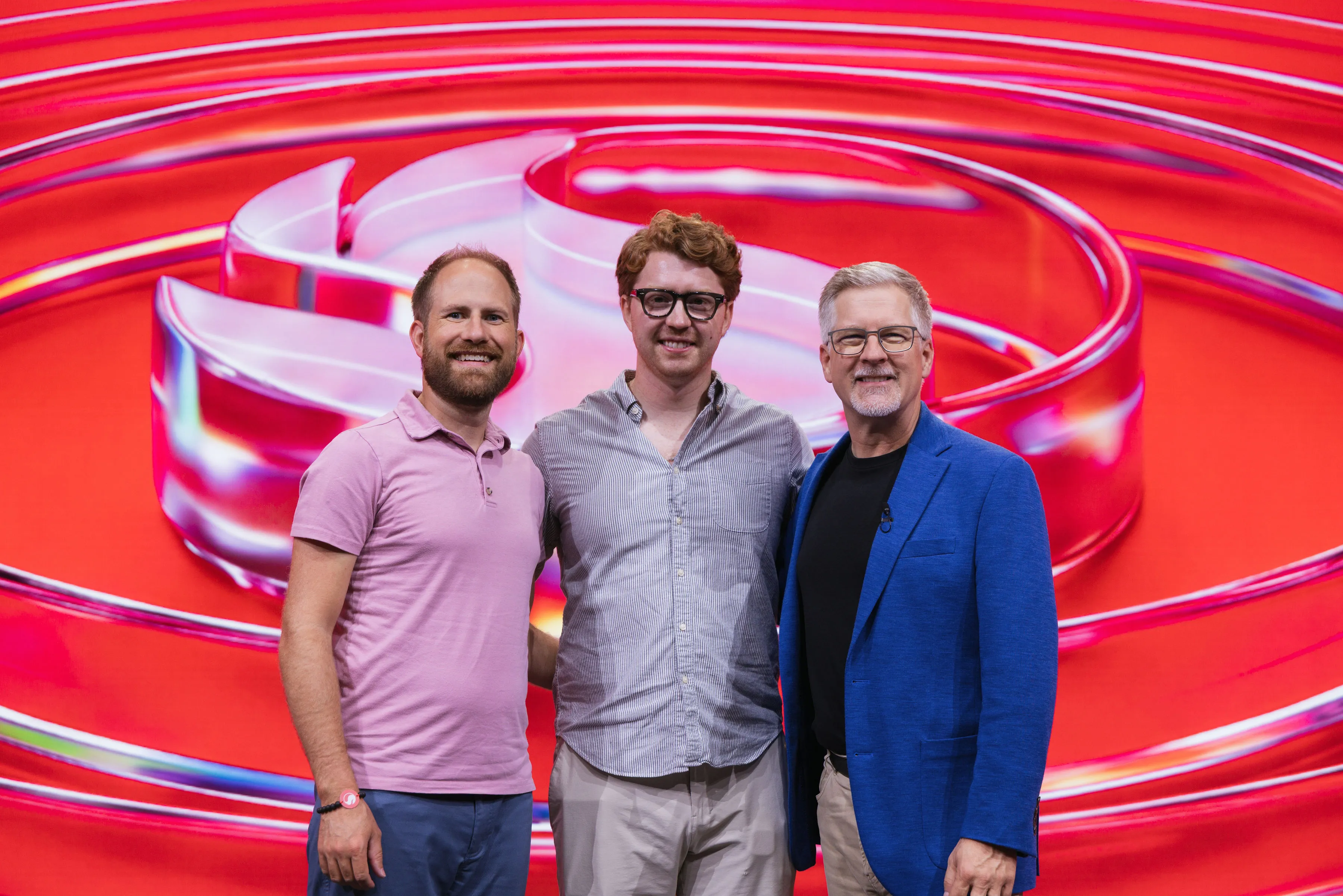 Joshua Timothy, Charley Beeman, and Judd Heape stand on the red Snapdragon Summit Stage with a glass Snapdragon logo behind them on screen